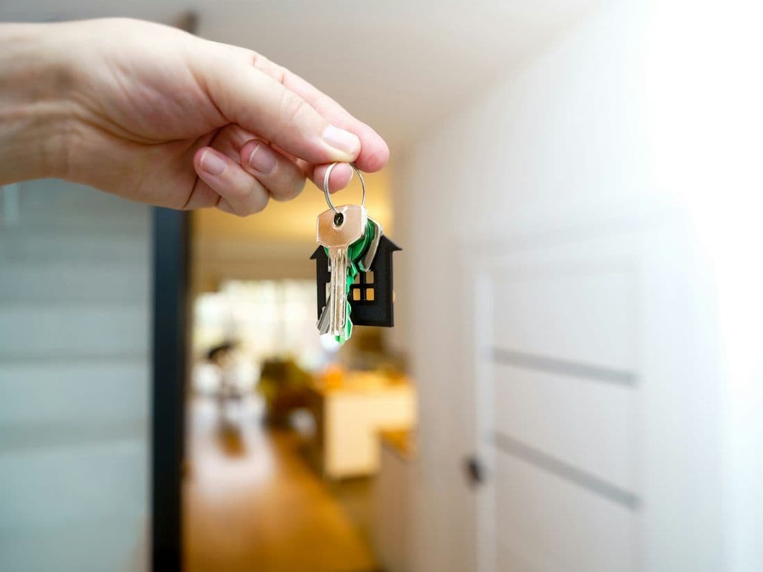 Mão segurando as chaves de uma casa na porta de entrada